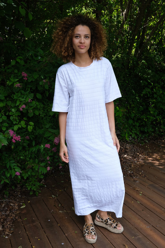 Woman standing in front of trees and bushes wearing a full length PRISM t-shirt dress