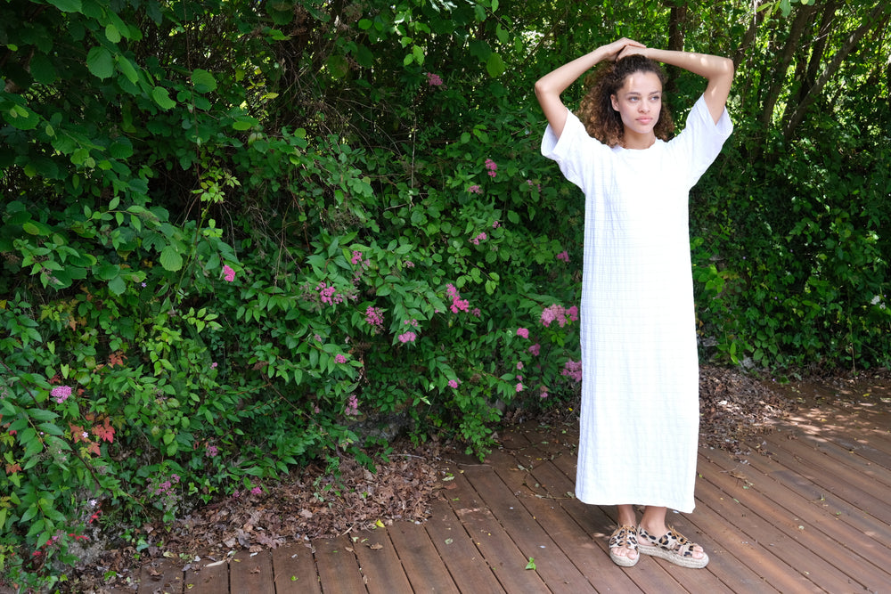 Woman standing in front of trees and bushes wearing a full length PRISM t-shirt dress